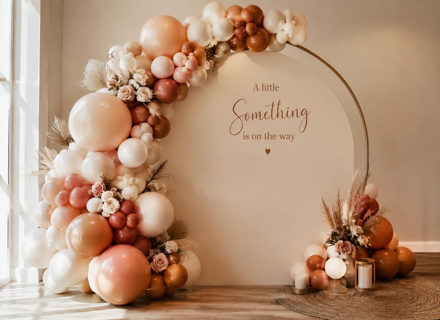 Balloon garland arch in cream, blush, and terracotta tones around a celebration backdrop